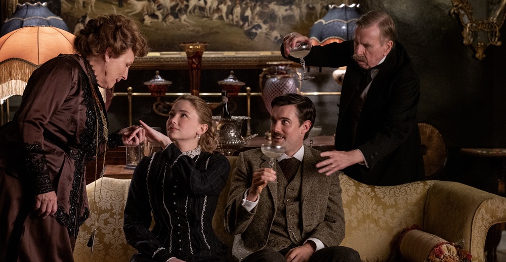 4 actors in period costume. 2 sitting on a sofa and two leaning over the sofa